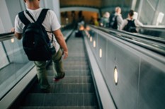 Man wearing rucksack walking down escalator