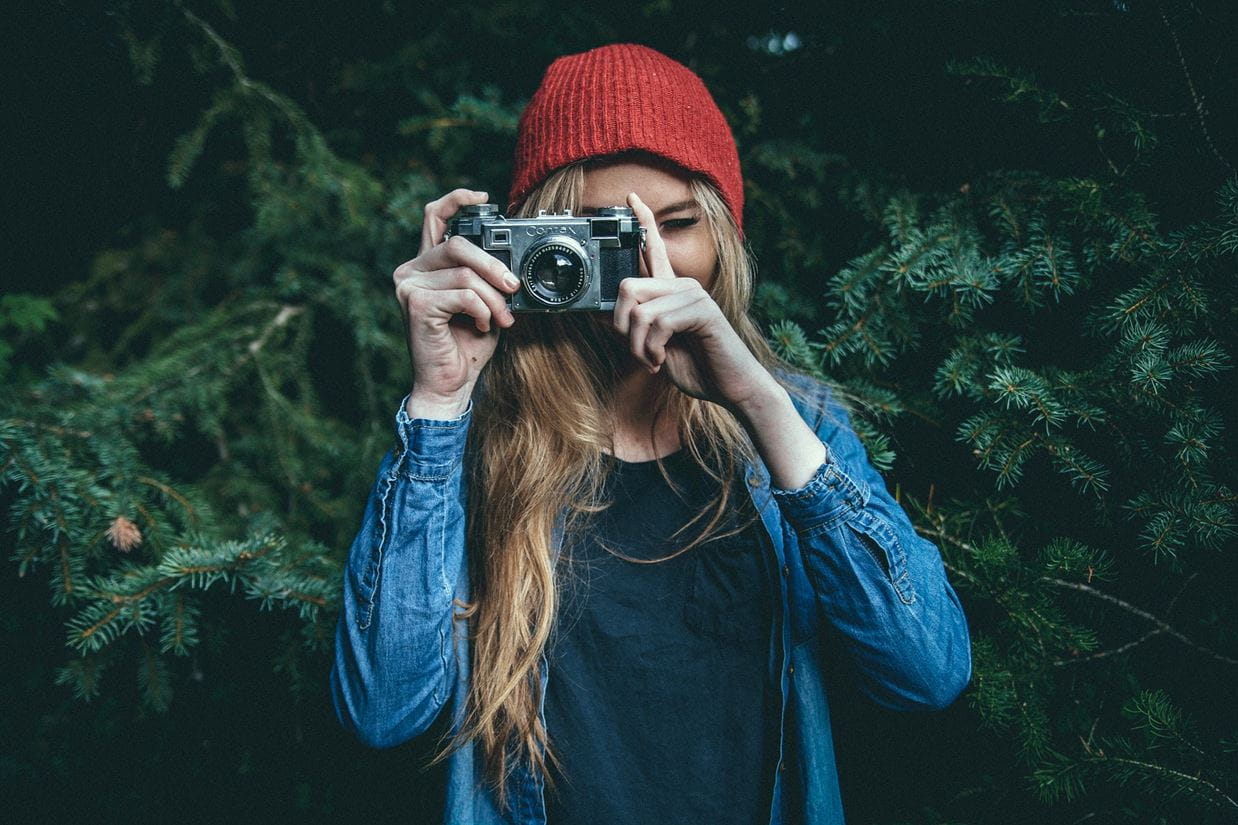 Young woman facing the camera taking a photo with an older style camera