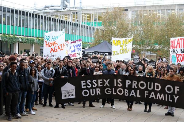 Students gathering on campus with large banner Essex is proud of our global family with the words - Essex is proud of our global family