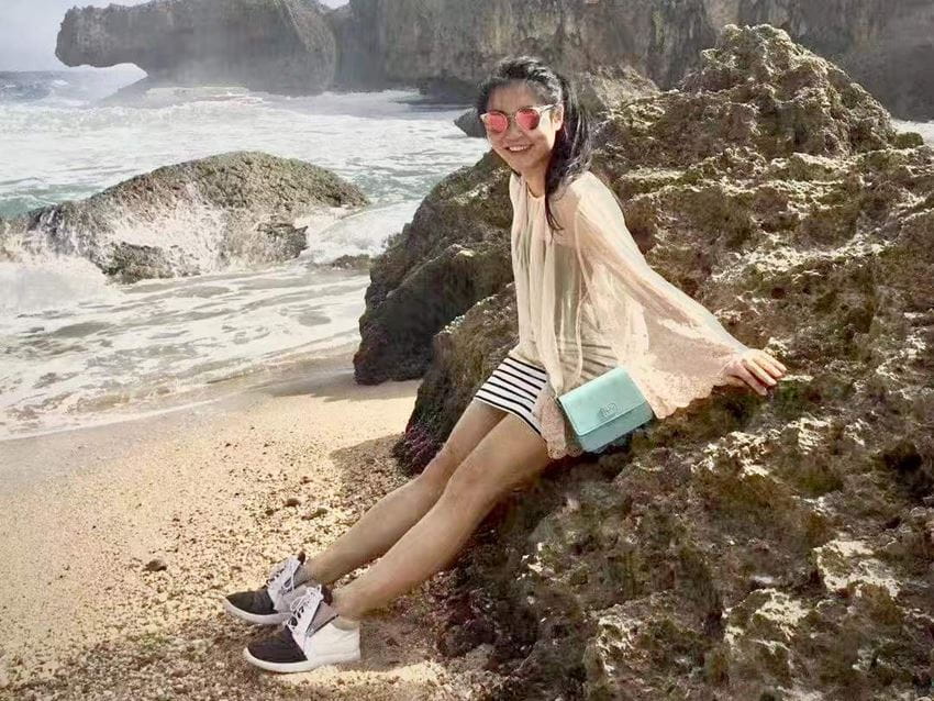 Du Li, 2010 MSc Accounting and Finance graduate, poses on a rocky beach wearing sunglasses and summer clothes. She is smiling beautifully.