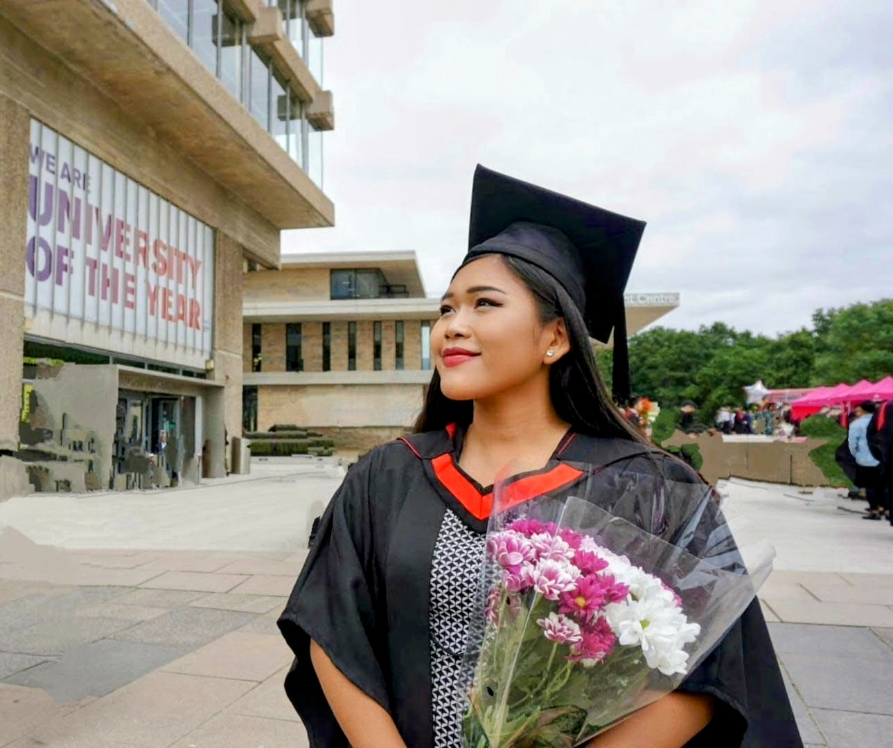 Fia Almanda wearing a graduation gown and holding flowers outside