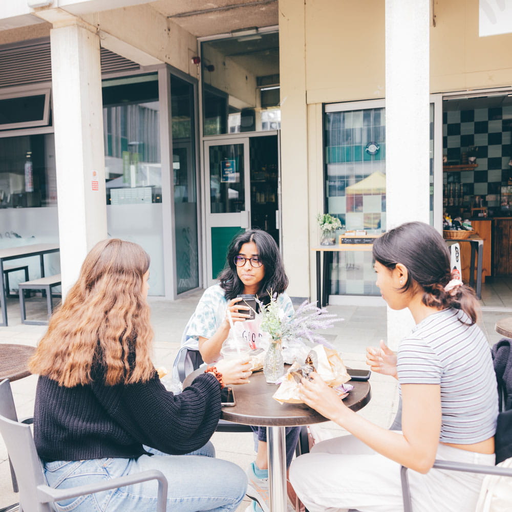 Students drinking and eating outside on the Colchester Campus squares