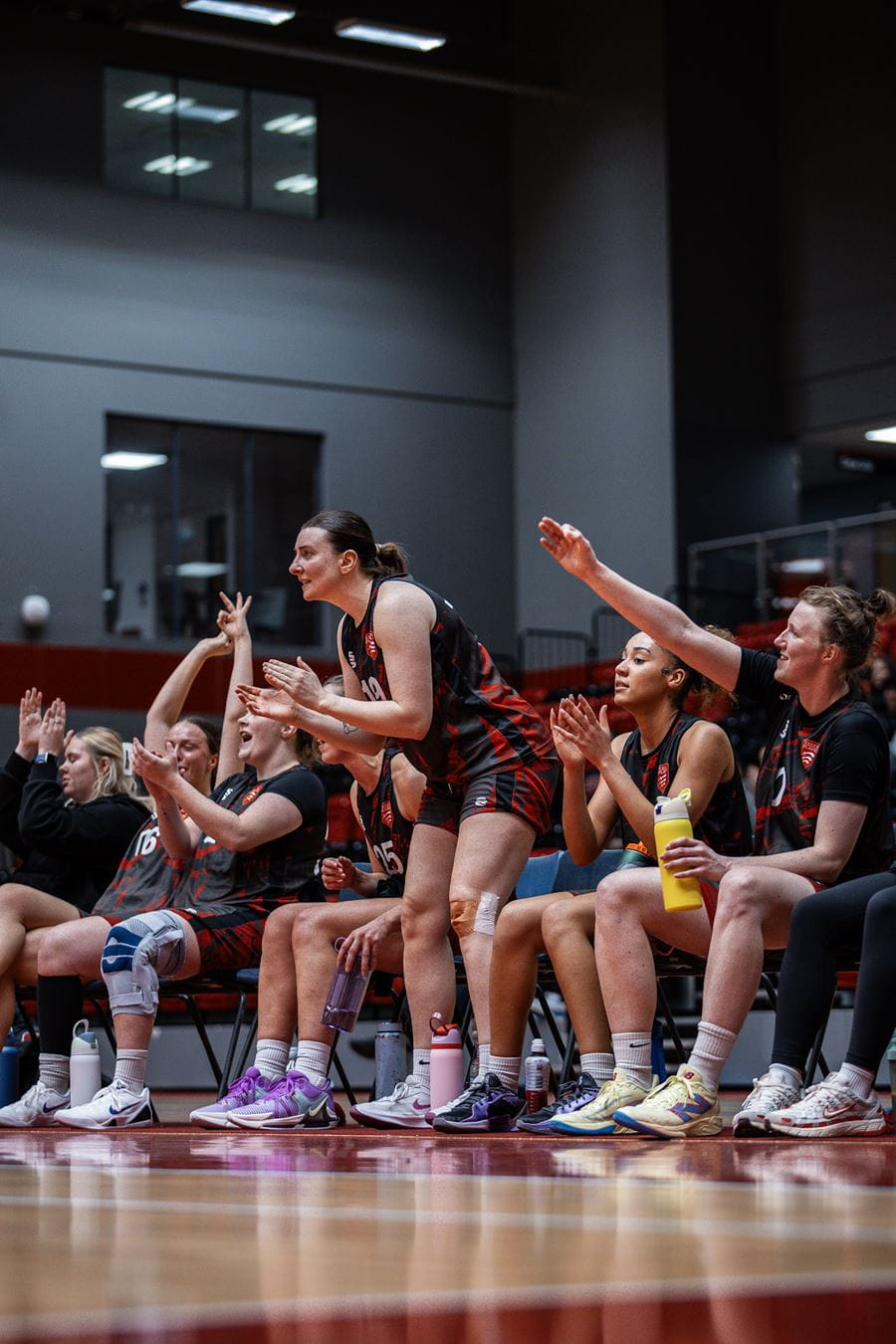 A group of females at the sidelines of a match cheering and clapping