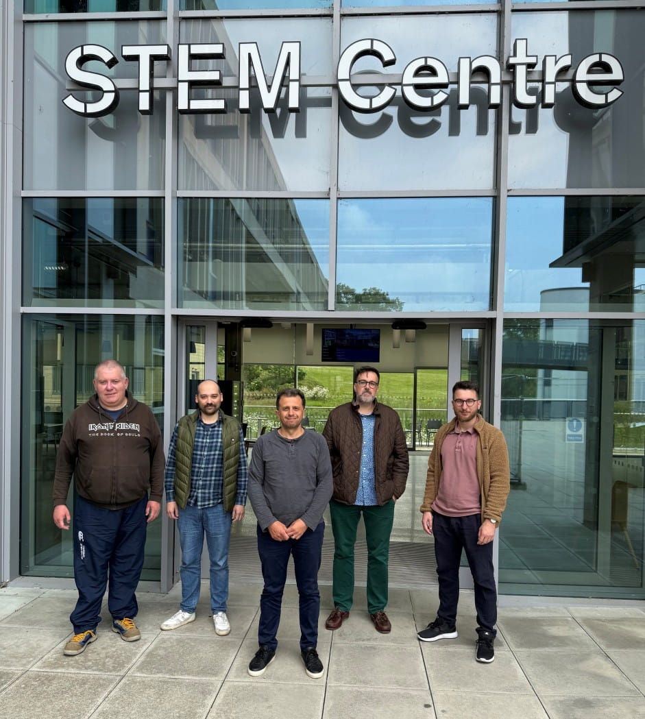 Five members of the Analysis and Mathematical Physics research group standing outside a large glass building with "STEM Centre" in large letters above them.