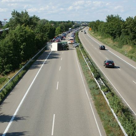 A motorway with an accident involving a tractor and a lorry on the left side, with a traffic queue trailing off into the distance.