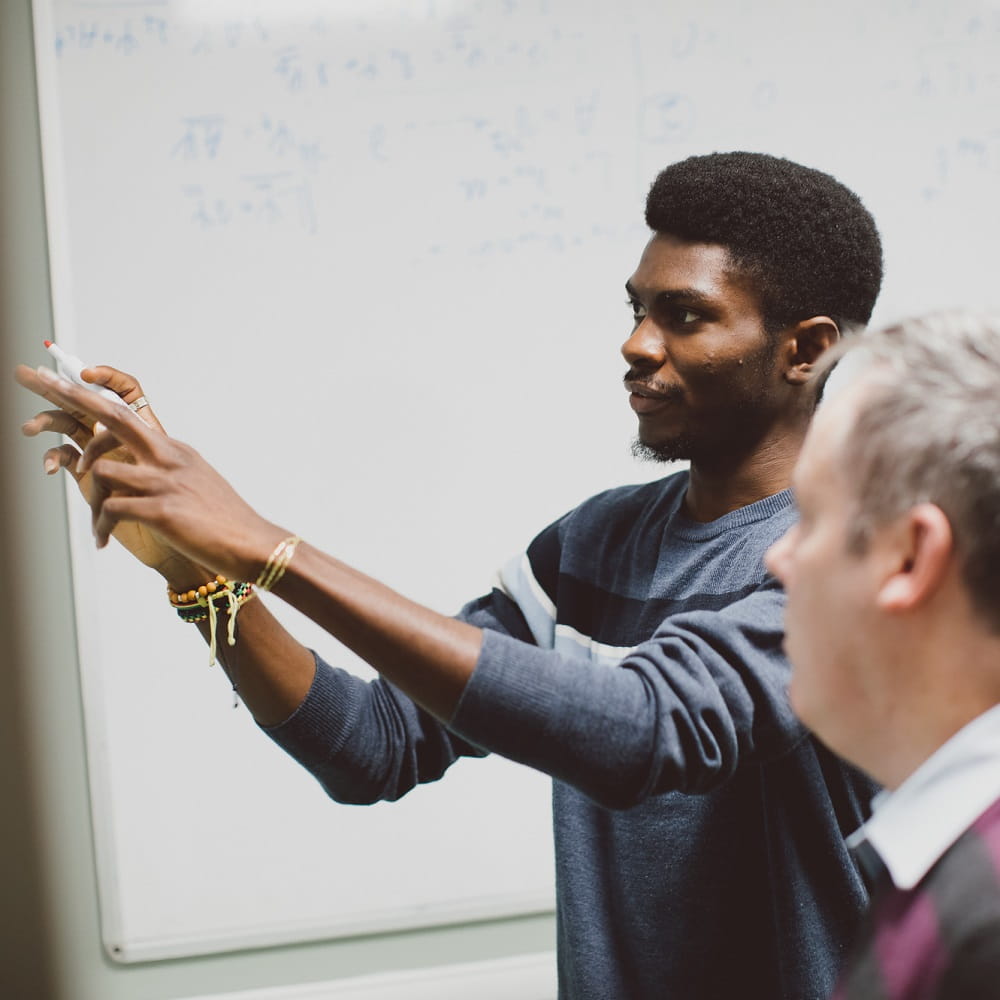 Student and academic working at a board together