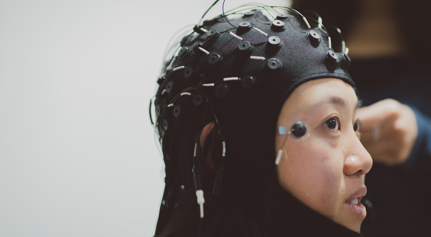 A profile shot of a student, facing the right side of the shot, wearing a large black EEG cap which covers the head and chin. 