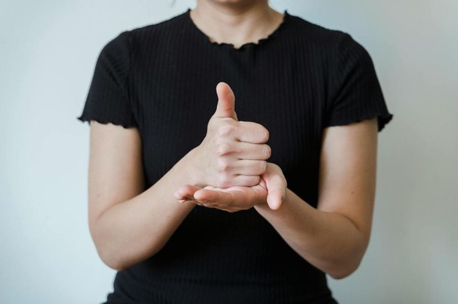 A person giving a thumbs up with their hand resting on an open palm. The person is wearing a black top.