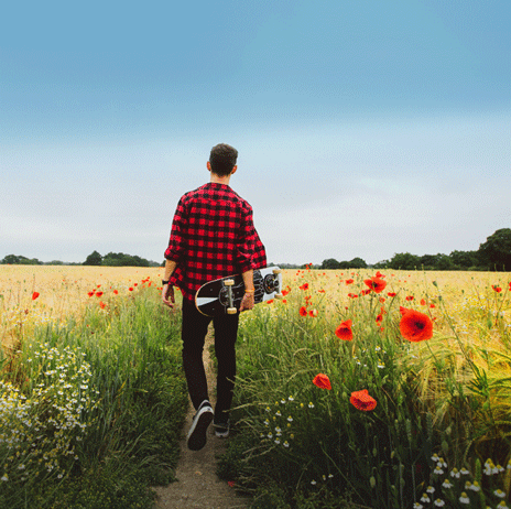 Man walking through poppy field holding skateboard