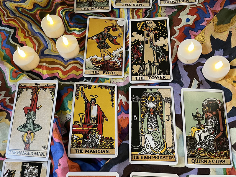 Tarot cards laid out on a colourful tablecloth: 'The Fool', 'The Tower', 'The Magician' and 'The High Priestess'.