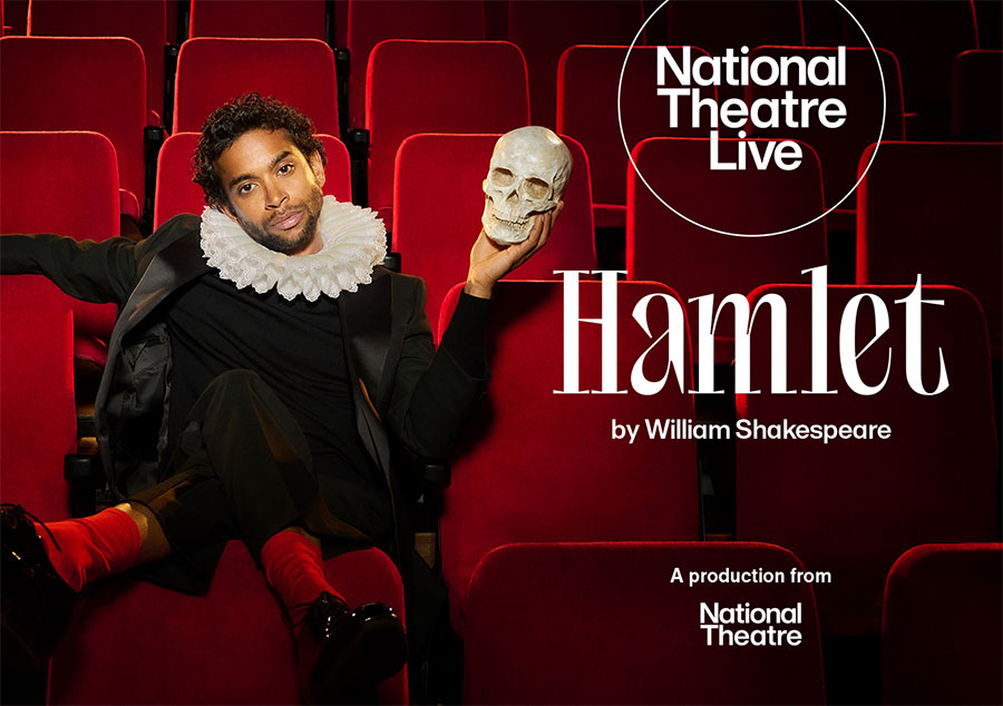 The National Theatre Live poster for 'Hamlet'. By William Shakespeare. Starring Hiran Abeysekera, who is wearing a collar ruff and a modern black suit, relaxingly sat in red, plush theatre seats, looking directly at the camera and holding a skull.