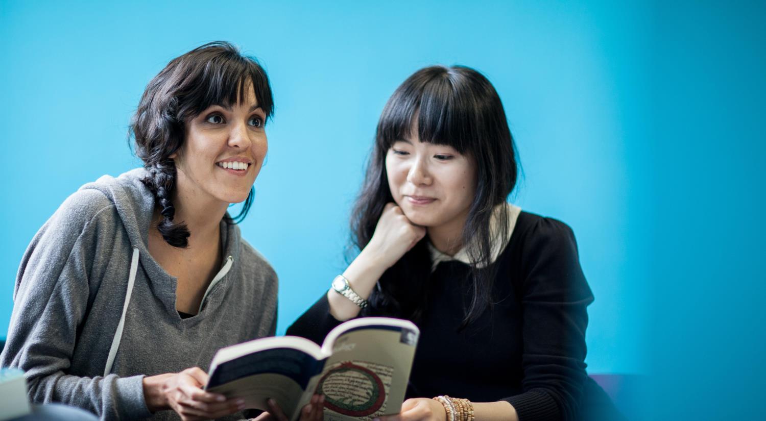 Two students peering over a book learning a language