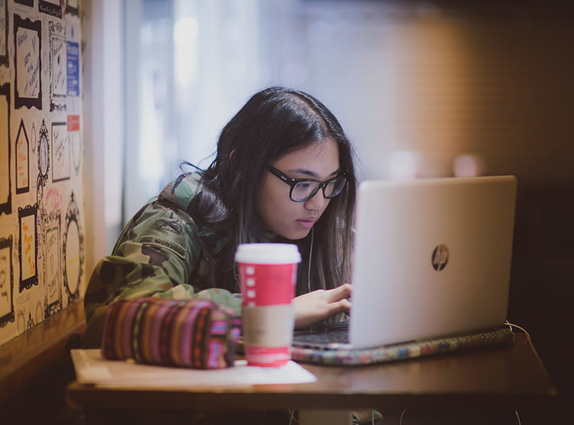 Female student working on her laptop at a table in a coffee shop