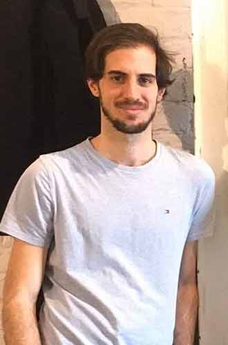 Andrea Lavio, wearing a white t-shirt and leaning against a brick wall