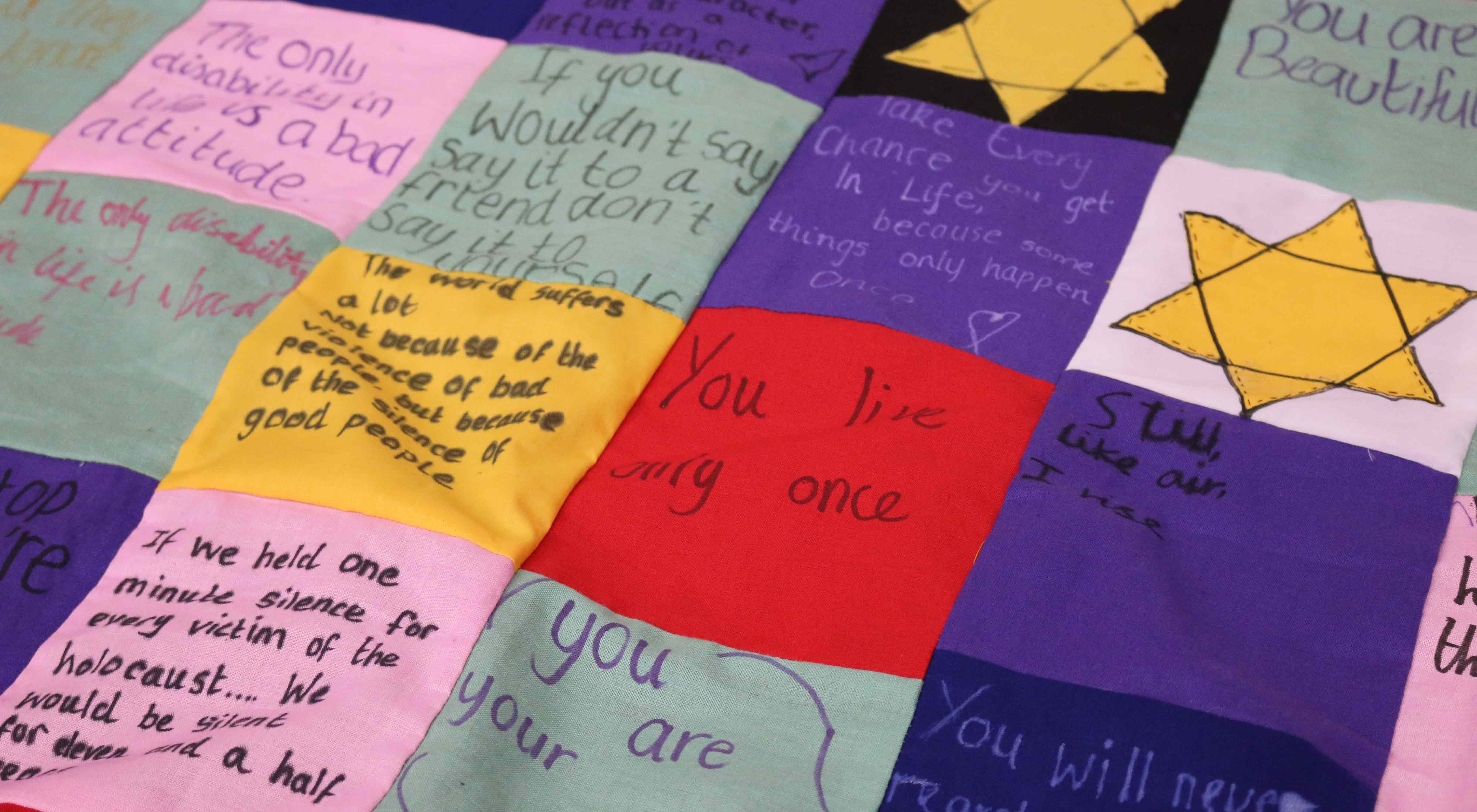 A colourful fabric quilt, stitched with words and images inspired by the Holocaust