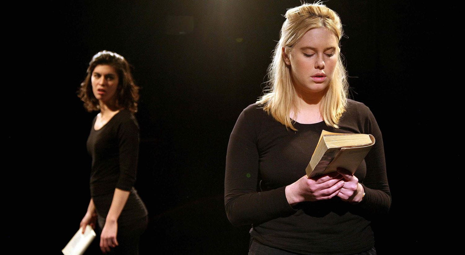 Two young girls, both wearing black, pictured on an empty stage, reading for a script