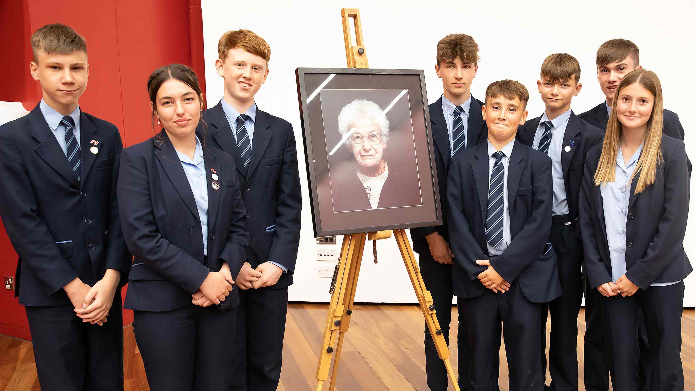 Pupils from Newmarket Academy standing alongside a framed portrait of Dora Love, which is standing on an easel 