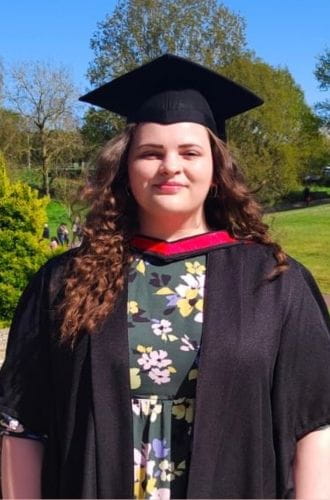 Student Ellie Hibbert, wearing her graduation gown and mortarboard on a sunny day