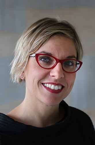 Paola Di Giuseppantonio Di Franco wearing a black top and red-rimmed glasses, smiling