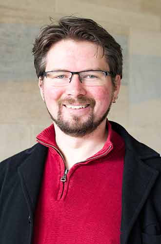 Dr Liam Jarvis, wearing glasses and a red jumper