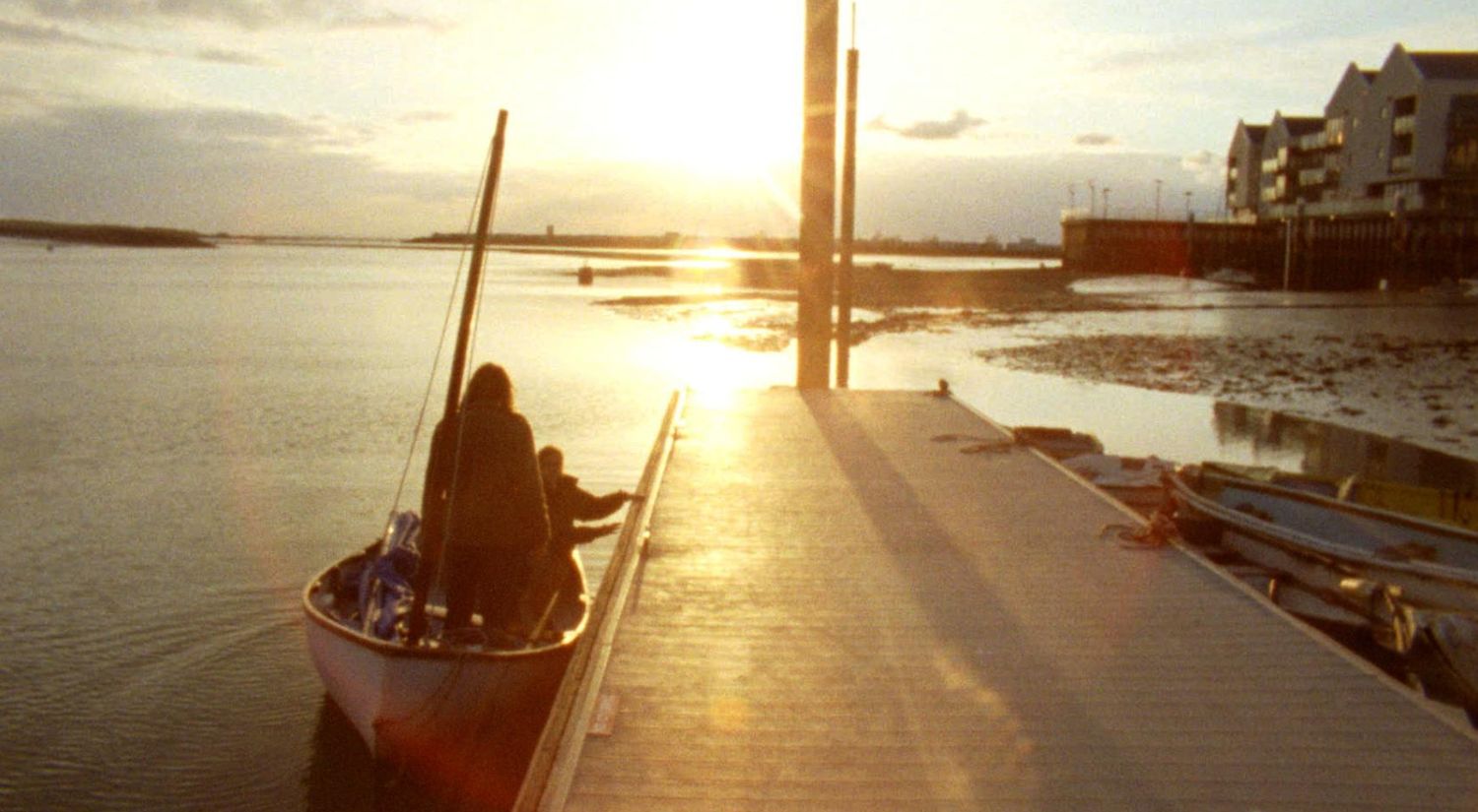 A couple on a small sailing boat are silhouetted against a sunset