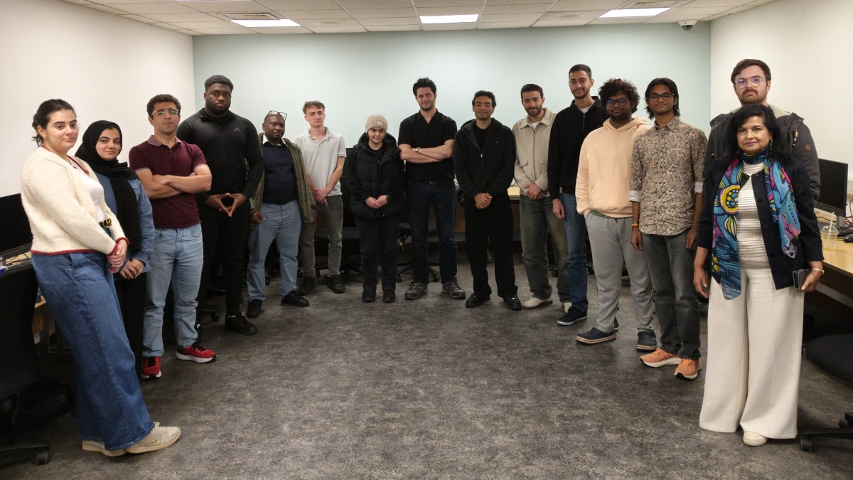 A group of people standing in a semi circle in a room, all looking at the camera.