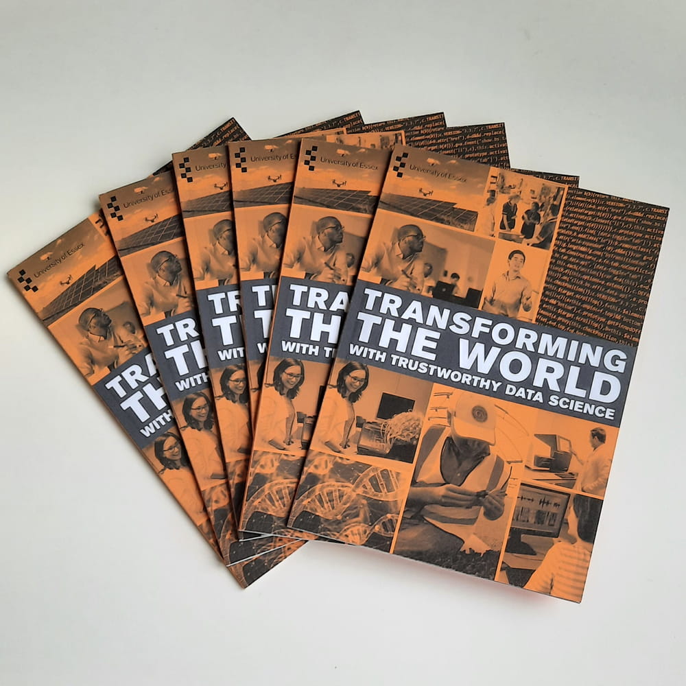 A fanned out pile of booklets with an orange cover and "Transforming the World" in white text on a grey banner.