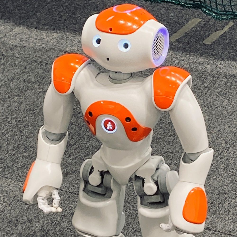 An orange and white "Pepper" robot, facing slightly to the left.