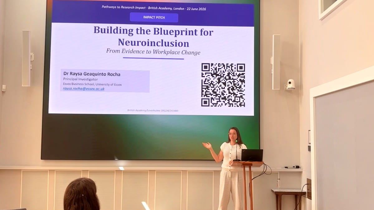 Dr Raysa Rocha standing in front of a screen delivering a presentation on "Building the blueprint for Neuroinclusion".
