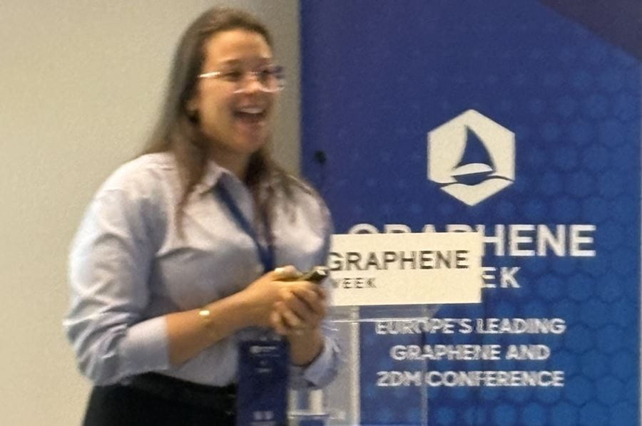 Dr Raysa Rocha standing in front of a sign about graphene week.