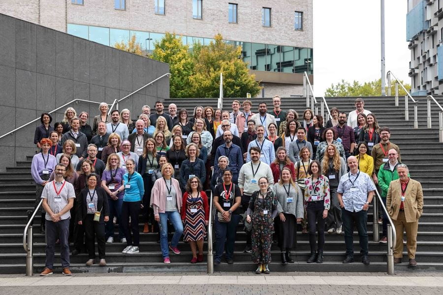 A large group of academics standing outside on some steps. All of them are looking at the camera.