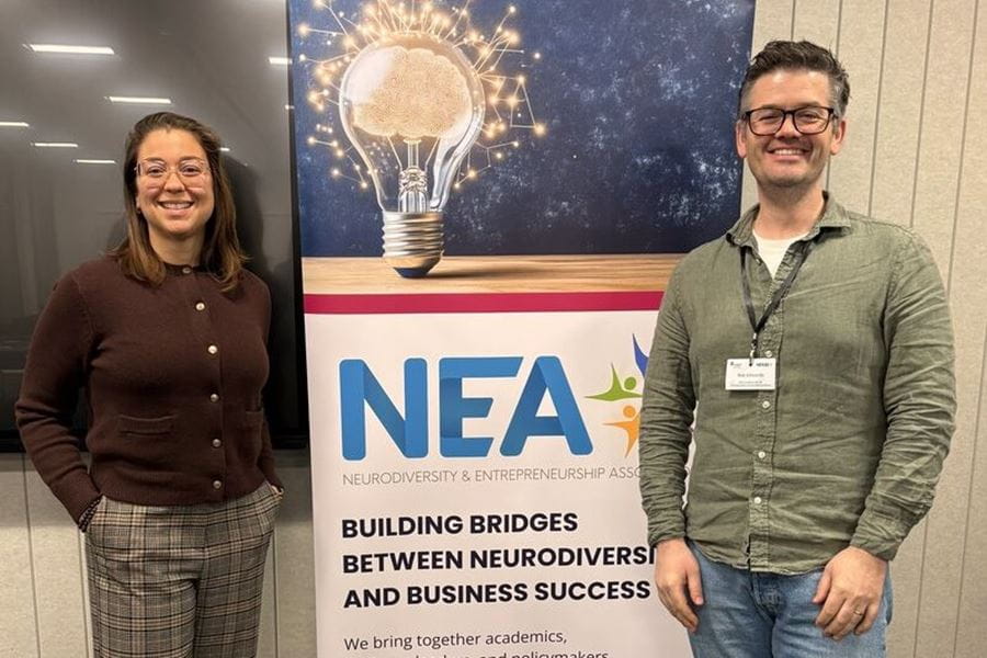 Dr Raysa Rocha standing next to a banner for the NEA conference, with another person standing on the other side.