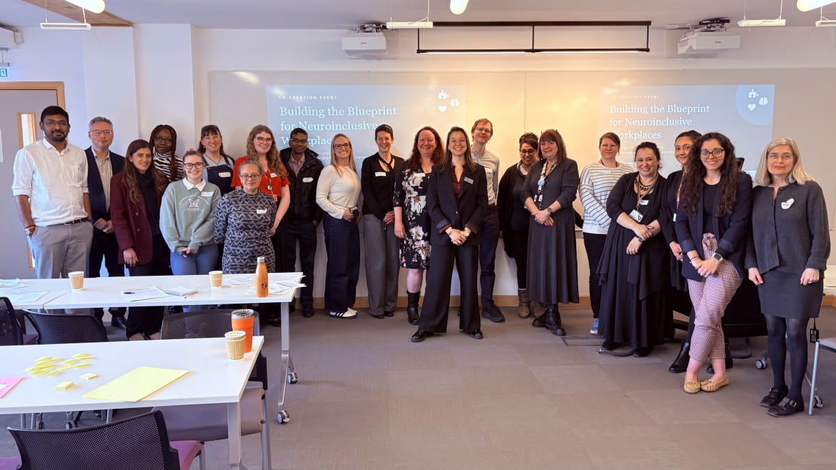 A group photo of the participants at a workshop on Neuroinclusive Workplaces, with several tables in the foreground.