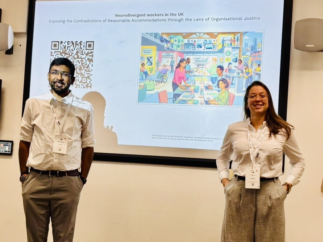 Dr Raysa Rocha (right) and Dr Siddhartha Saxena (left) standing in front of a screen showing a slide from their presentation.