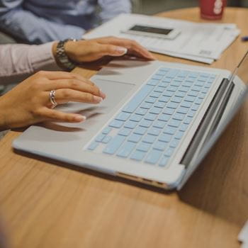 A laptop on a desk, with a pair of hands near the keyboard.