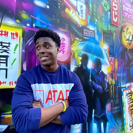 Photo of Theo Dwumah in an urban environment with neon lights behind him
