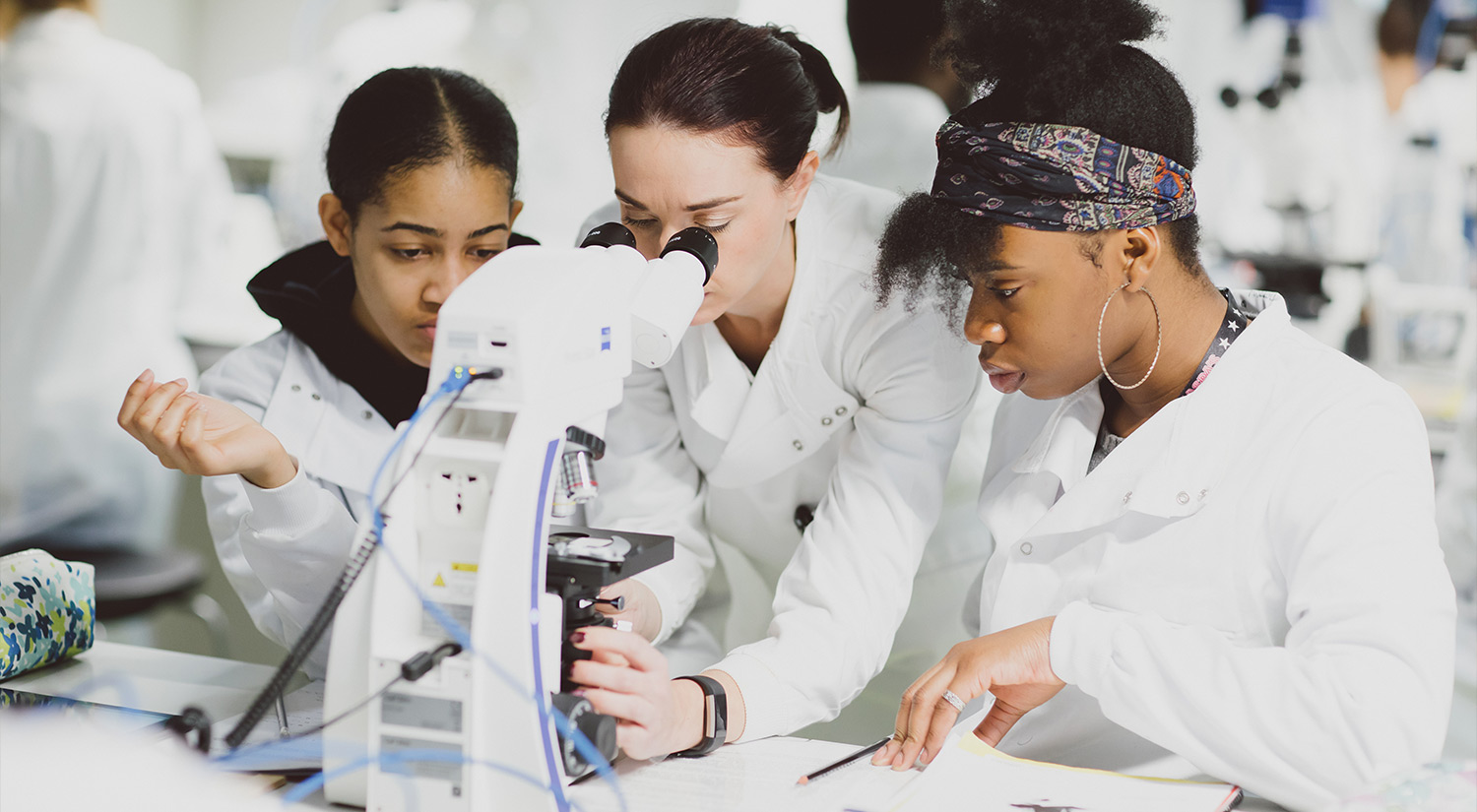 Two students and member of staff in a lab using a microscope