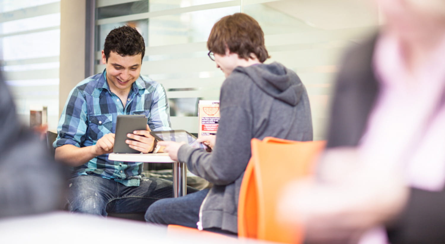Image of two students working together on their tablets in a cafe