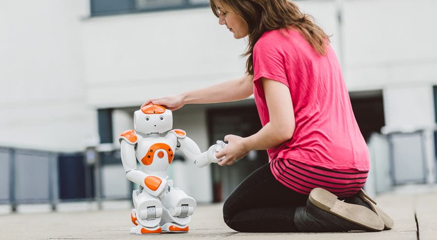 Image of a female student testing a Nao robot outside the computer science building