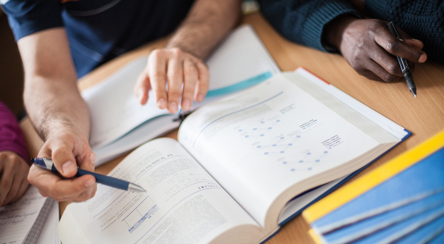 Image of people working together over a collection of textbooks on a desk