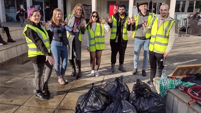 A group of students wearing high visibility jackets standing with some black bin bags of rubbish from a litter pick