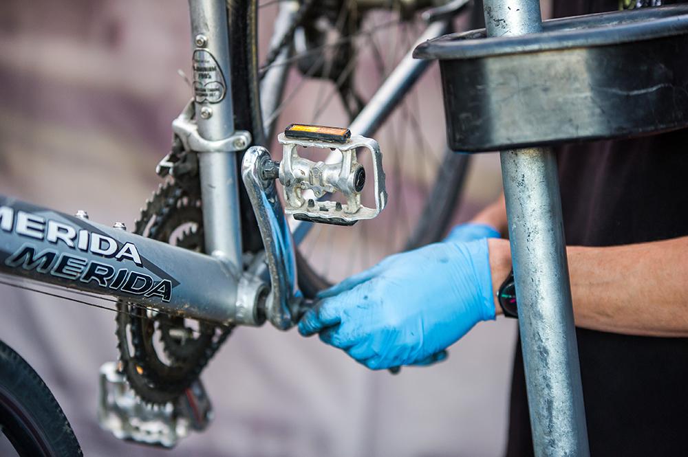 A gloved hand repairs the pedals of a bike.