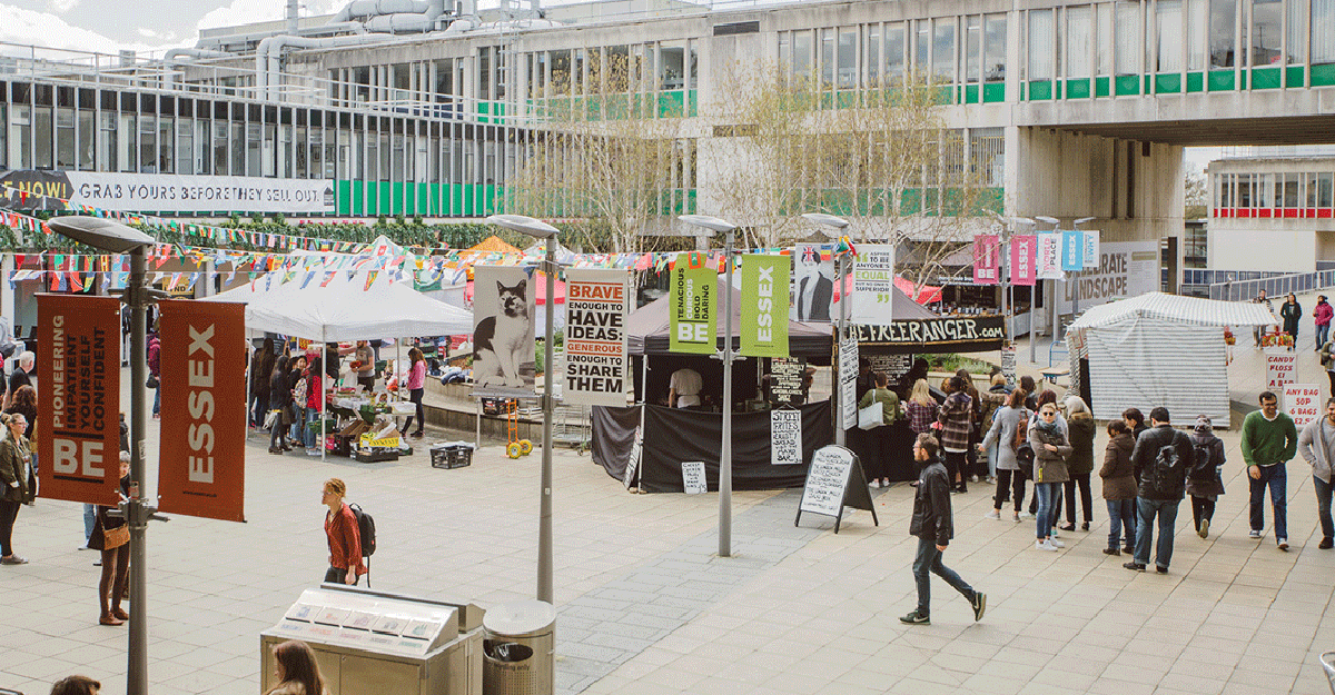 A busy image of life on our campus squares with market stalls and people walking about