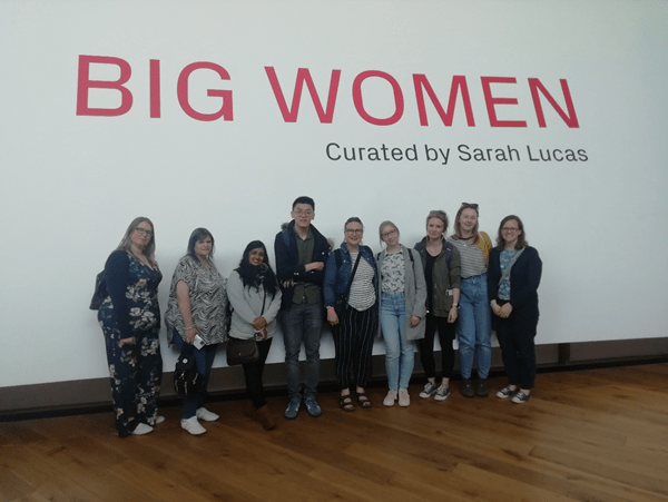 photo of students standing infront of a banner BIG WOMEN exhibition curated by Sarah Lucas