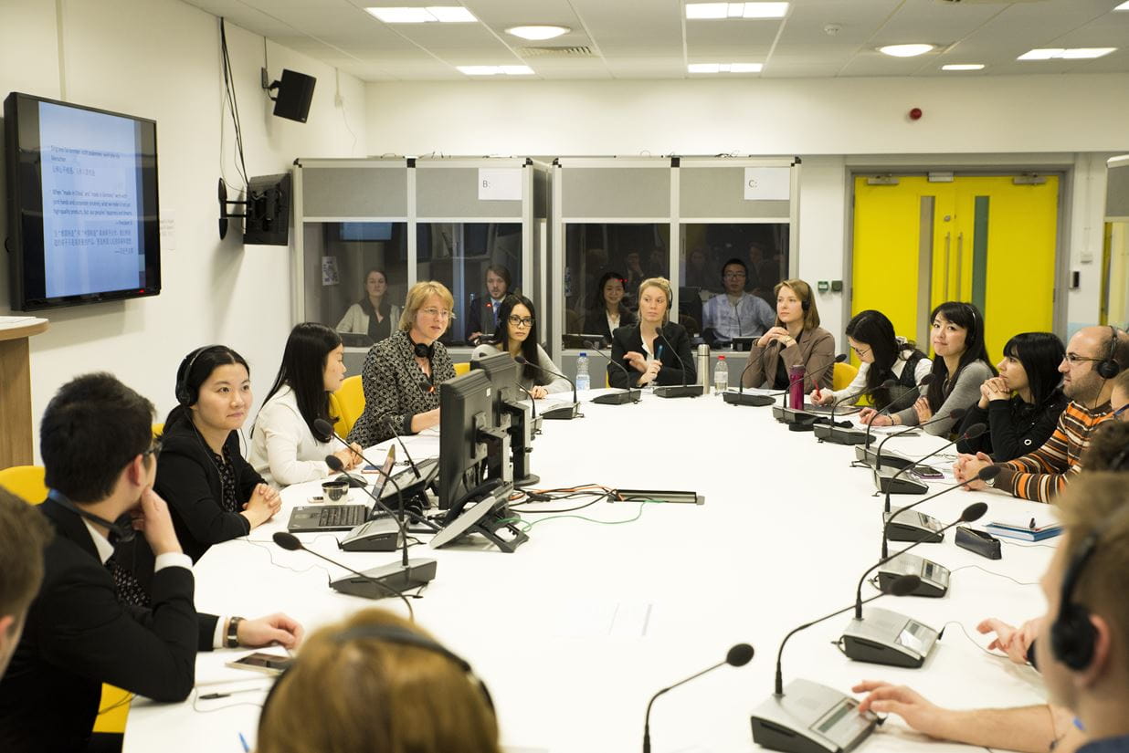 Students taking part in a mock conference within our interpreting lab - students sitting around a round table, with microphones and interpreting equipment