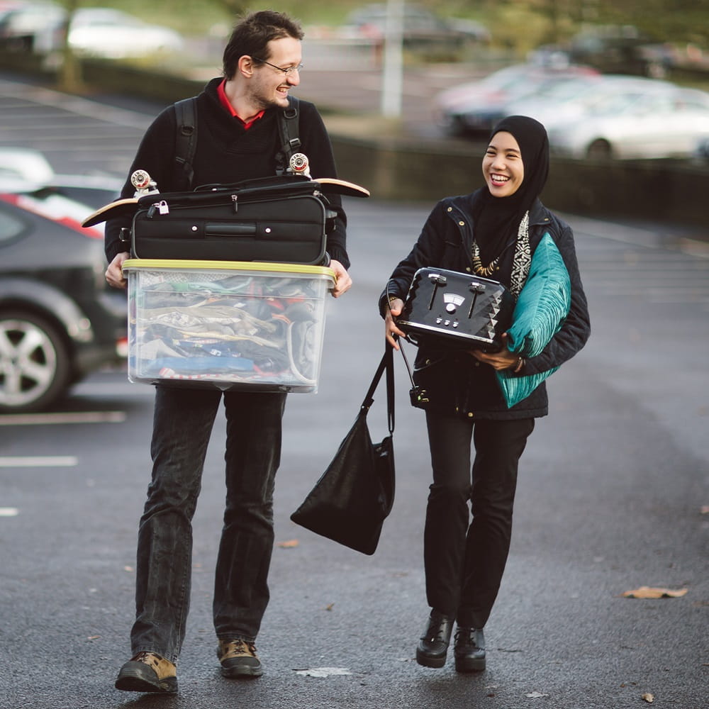 Two students walking together with boxes and other bits for moving in