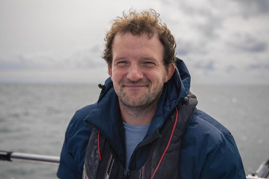 Thomas Stamp profile picture on a boat with a grey sky and sea behind him