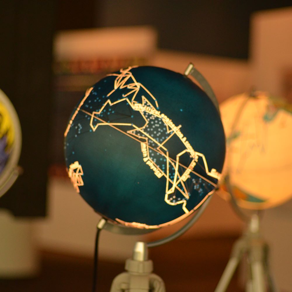 Picture of three miniature globes on stands, with one in focus and two others out of focus, all lit up by blue, white and green colours with a candlelit tone over the image