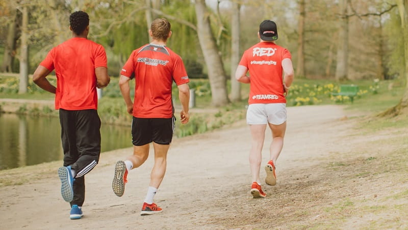 Three men, all wearing red t-shirts, running along a path away from the camera.
